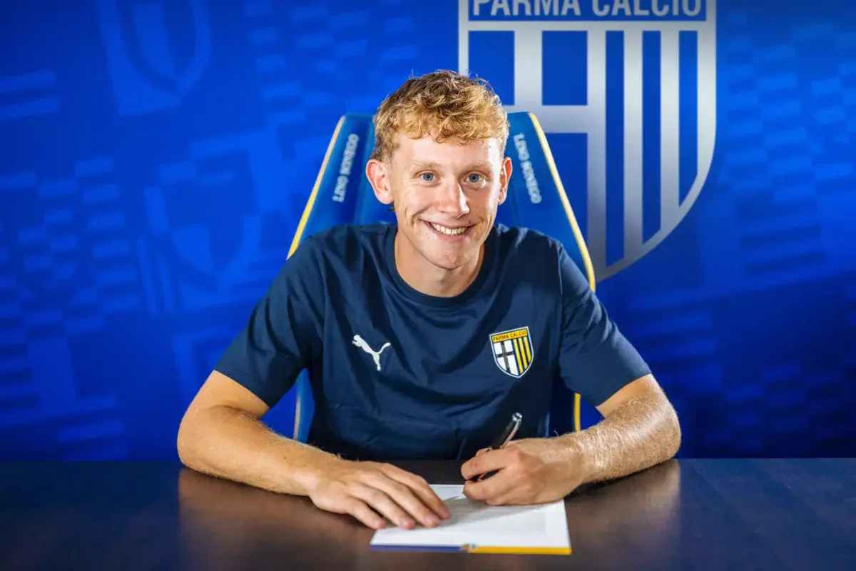 Oliver Sorensen smiling while signing a contract in front of a Parma Calcio backdrop