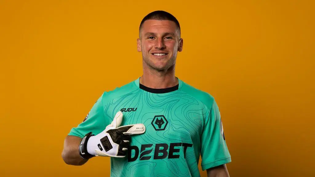 Sam Johnstone smiling in a green Wolverhampton Wanderers goalkeeper kit against a yellow background