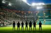Seven footballer silhouettes at a floodlit Celtic Park-style stadium for a Europa League squad announcement