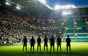Seven footballer silhouettes at a floodlit Celtic Park-style stadium for a Europa League squad announcement