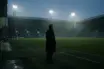 Silhouetted football manager facing an empty green pitch under stadium lights after a difficult run of defeats